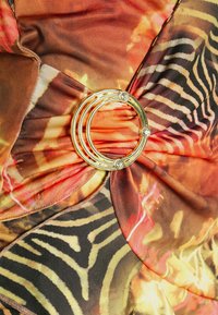 Tecido multicolorido com uma combinação de padrões florais e listras de tigre. Apresenta um acento circular dourado com strass ao centro.