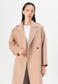Hellbrauner Wollmantel mit eingekerbtem Kragen, doppelt knöpfbare Vorderseite und weiten Ärmeln. Hat ein schickes Design und einen strukturierten Stoff.
