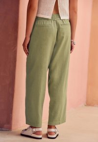 Lysegrønne, løstsiddende bukser med tekstureret stof, der har høj talje og to baglommer, kombineret med hvide sandaler.