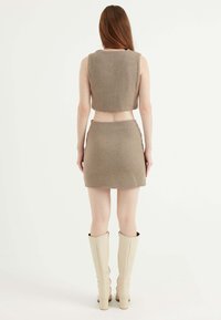 Brunt herringbone stickad set som inkluderar en kort topp och en mini kjol, kompletterad med knähöga beige stövlar. Slät textur.