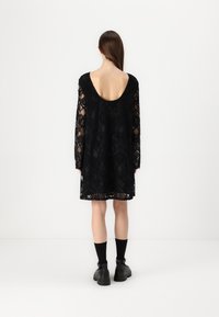 Svart spetsklänning med långa ärmar, urveckad rygg och intrikata geometriska mönster. Bärs med svarta ankelstövlar och strumpor.