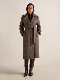 Cappotto di lana a quadri marrone con cintura, ampie rever, e due tasche frontali. Stivali bordeaux lucidi al ginocchio con punta affusolata.