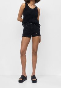 Canotta nera a costine, pantaloni shorts in denim nero a vita alta con orlo sfrangiato e dettagli strappati, abbinati a sandali neri a scivolo spessi.