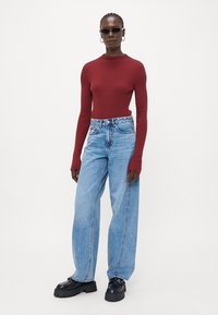 Ribbed bordó hosszú ujjú felső, világoskék, oversized farmernadrággal párosítva. A modellen fekete, vastag talpú cipő és napszemüveg található.