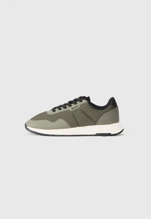 Sneakers verzi din plasă cu accente negre, parte superioară texturată, șireturi plate și o talpă albă, cu caneluri. Logo-ul este afișat pe lateral.
