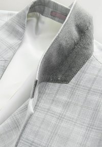 Blazer de cuadros gris claro con cuello de fieltro, forro de satén suave y costuras detalladas a lo largo de los bordes. Destaca por sus líneas y texturas limpias.