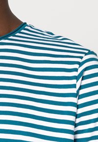 Camisa de manga larga a rayas en verde azulado y blanco, con un cuello redondo y una textura suave de algodón. Las rayas horizontales están espaciadas de manera uniforme.