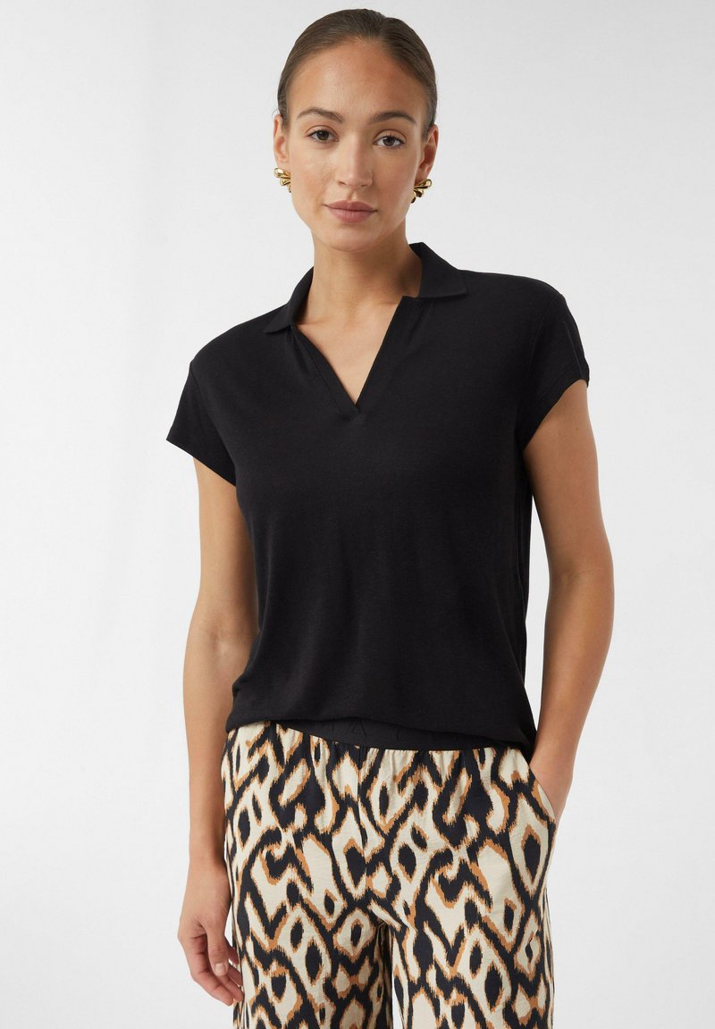 Czarna, krótki rękaw polo z dekoltem w serek i luźnym krojem. Gładka faktura, w połączeniu z szerokimi spodniami z nadrukiem o abstrakcyjnym wzorze.