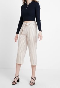Černý dlouhý rukáv cropped top s detaily na zipu spárovaný s béžovými a bílými pruhovanými širokými kalhotami se zavázaným pasem. Černé sandály na podpatku.