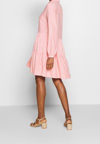 Abito rosa a righe con maniche lunghe, un corpino aderente e una gonna a strati. Abbinato a sandali con tacco quadrato beige.