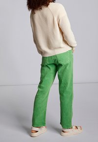 Ljus beige stickad tröja och klara gröna raka jeans. Jeans har en något urbleknad textur. Skorna är i en ljus färg med remmar.