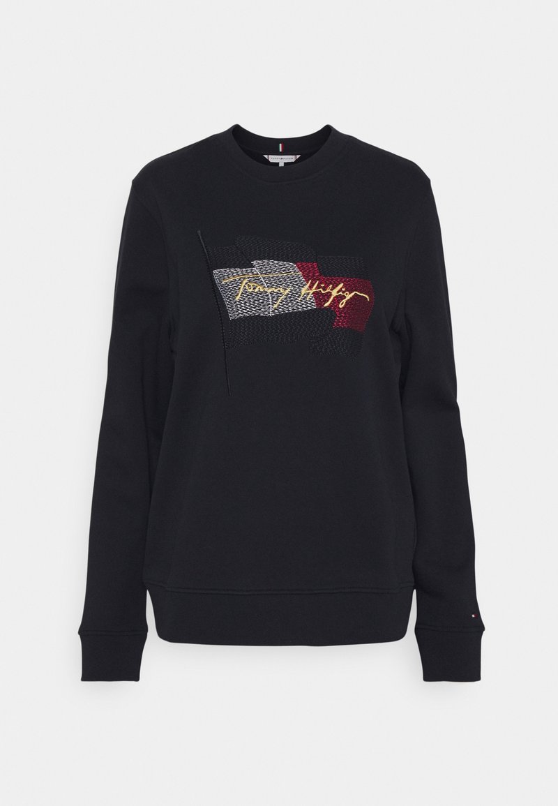 Sweat-shirt noir à manches longues avec col rond, drapeau Tommy Hilfiger et signature brodés en rouge, blanc, noir et jaune sur le devant.