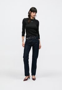 Svart ribbestrikket langermet topp, mørkeblå jeans med rette ben og burgunder spisse hæler. Enkelt design med minimale metalliske detaljer.