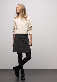 Kremowy wełniany sweter z wysokim kołnierzem; szara, teksturowana spódnica w kształcie litery A; czarne kryjące rajstopy; czarne botki za kostkę. Prosta, nowoczesna sylwetka w neutralnych kolorach.