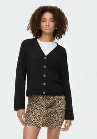 Cardigan nero con scollo a V, chiusura con bottoni e bordi a costine, abbinato a una gonna in stampa leopardata, con texture liscia e design aderente.