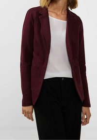 Burgundy blazer med skräddarsydd passform, slagkrage, långa ärmar och två framfickor, i kombination med en vit blus och svarta byxor.