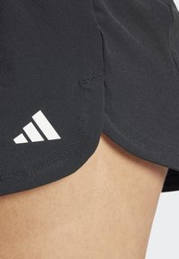 Pantalones cortos deportivos negros hechos de tejido ligero, que presentan un logo de Adidas de tres rayas blancas en el dobladillo y un diseño curvo y dividido.