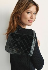 Czarna torebka z lakierowanej skóry z pikowanym teksturem i złotymi elementami, z górnym zamkiem błyskawicznym i pasem na ramię, noszona na krzyż.