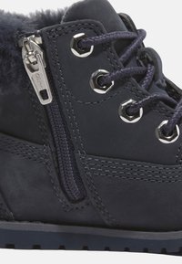 Bota de invierno azul marino con ojales de metal, cordones gruesos, cremallera lateral, costuras detalladas y un suave collar de piel.