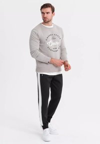 Grijze sweatshirt met witte print, zwarte broek met witte strepen en witte sneakers. Casual fit. Glad textuur, eenvoudig ontwerp.
