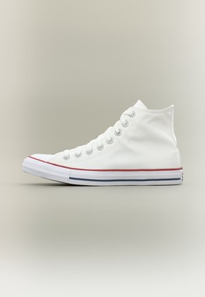 Basket montante en toile blanche avec lacets blancs, semelle en caoutchouc et rayures rouges et bleues sur un fond neutre.