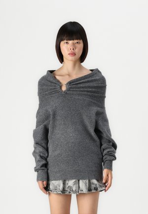 Pull gris surdimensionné avec un col froncé et un accent circulaire. Texture douce, manches longues, associé à une jupe en denim.