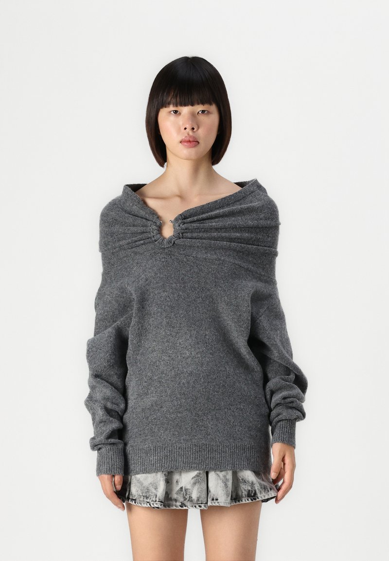 Suéter gris de gran tamaño con un cuello fruncido y un acento circular. Textura suave, mangas largas, combinado con una falda de mezclilla.