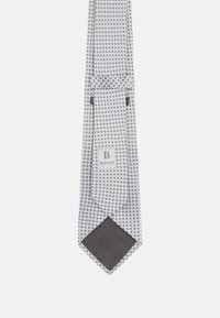 Noeud papillon blanc avec un motif géométrique en gris et bleu marine. Présente une pointe en gris foncé uni et une étiquette de marque près de l'extrémité étroite.