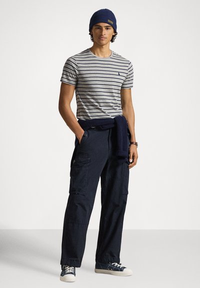 Γκρι ριγέ μπλούζα, ναυτικό μπλε παντελόνι cargo με τσέπες και μπλε πλεκτό σκουφάκι. Λευκά αθλητικά παπούτσια με μπλε λεπτομέρειες. Καθημερινή εμφάνιση.