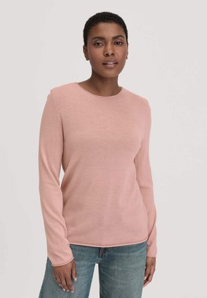 Hellrosa, langärmliger Strickpullover mit rundem Halsausschnitt und gerippten Bündchen, kombiniert mit blauen Jeans. Weiche Textur, enganliegendes Design.