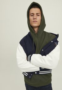 Hoodie in Olivgrün mit einem Navy- und Weißton Varsity-Jacke Overlay.  Mit gerippten Bündchen und Druckknopfverschluss.