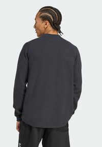 Dark gray long-sleeve shirt with a textured, waffle-knit pattern and a rounded hem, worn with black pants.