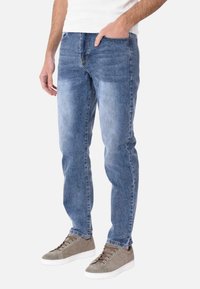 Jeans in denim azzurro chiaro con taglio dritto, caratterizzati da un lavaggio sbiadito, design a cinque tasche e dettagli cuciti, indossati con sneakers grigie.