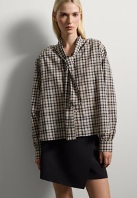 Cream and navy plaid button-up shirt with a tie collar and long sleeves, paired with a black asymmetrical skirt. Smooth fabric texture.
