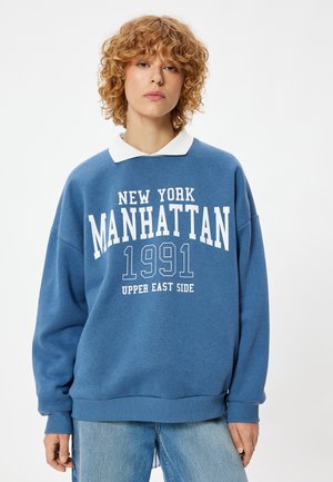 Felpa blu con scritte bianche "NEW YORK MANHATTAN 1991 UPPER EAST SIDE," con colletto bianco e design morbido.