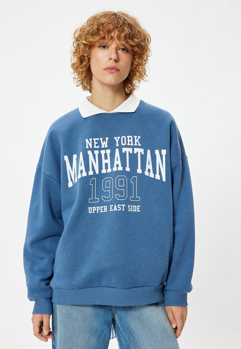 Blauwe sweatshirt met witte lettering "NEW YORK MANHATTAN 1991 UPPER EAST SIDE," met een witte kraag en een losse pasvorm.