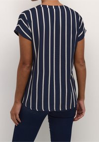 Haut bleu marine à manches courtes avec des rayures verticales crème, col rond et ourlet incurvé. Tissu lisse avec une coupe décontractée.