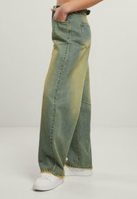 Vide bukser i en gradient af grønne nuancer, med en frynsede kant og klassisk fem-lomme design. Sammen med hvide sneakers.