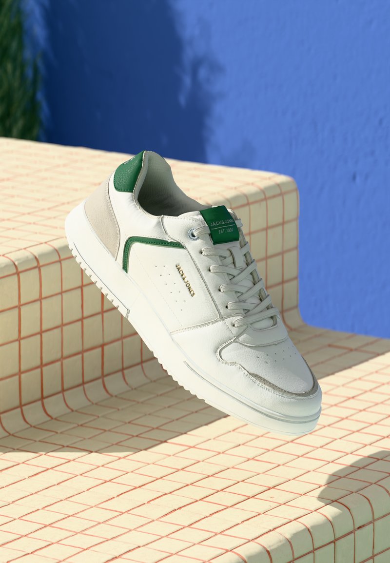 Fehér bőr sneaker zöld és szürke részletekkel. Lyukacsos díszítéssel, lapos fűzős kialakítással és texturált gumi talppal rendelkezik.