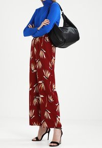 Blå långärmad topp med detalj vid halsen, röda blommönstrade vida byxor, svart läderaxelväska och svarta högklackade sandaler.