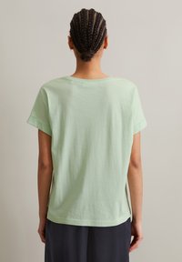 Hellgrünes Baumwoll-T-Shirt mit kurz gerollten Ärmeln, lockerer Passform und rundem Halsausschnitt. Schlichtes Design, weiche Textur, keine sichtbaren Muster.