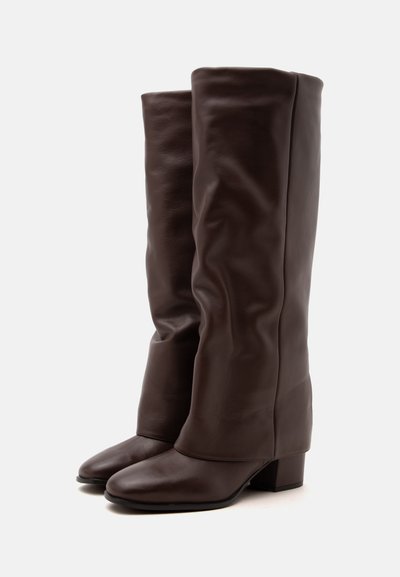 Bottes hautes en cuir marron foncé avec bouts carrés et talons bas épais, debout sur un fond clair uni.