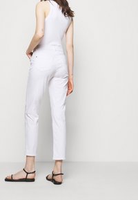 Bílé džíny z denimu s úzkým střihem, zkrácenou délkou a zadními kapsami; nošeny s bezrukávovým bílým topem a černými plochými sandály.