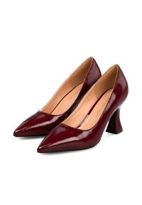 Un par de brillantes tacones altos de punta en rojo oscuro con tacones de bloque acampanados y forro interior beige sobre fondo blanco.
