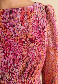 Multifarbener Stoff mit einem lebendigen Muster aus pinken, orangefarbenen und lila Formen, das eine subtile Textur aufweist und an der Schulter gerafft ist.