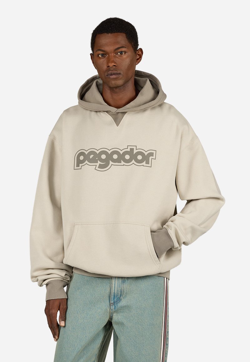 Μπεζ φούτερ με μεγάλο γκρι λογότυπο "pagador", καγκουρό τσέπη και αντίθεση γκρίζα επένδυση στη κουκούλα. Χαλαρή εφαρμογή με ριμπ μανσέτες.
