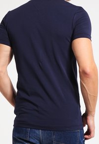 Camiseta ajustada de color azul marino, hecha de algodón suave, de mangas cortas, con un escote en forma de V y detalles de costura sutiles en la parte posterior.