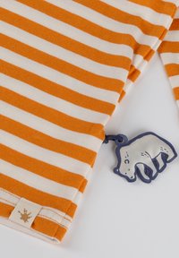 Gestreiftes Oberteil mit orange-weißen horizontalen Streifen, einem Etikett mit einem Logo und einem bärchenförmigen Anhänger in Weiß und Marineblau.