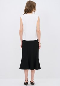 Hvid ærmeløs bluse parret med en sort, svajende nederdel. Blusen har et enkelt design, mens nederdelen har en flydende struktur ved kanten.