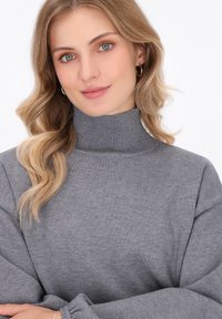 Grauer Rollkragenpullover mit geripptem Kragen und Bündchen, bietet eine weiche Textur und einen lockeren Schnitt. Nahaufnahme konzentriert sich auf den Ausschnitt und den Stoff.